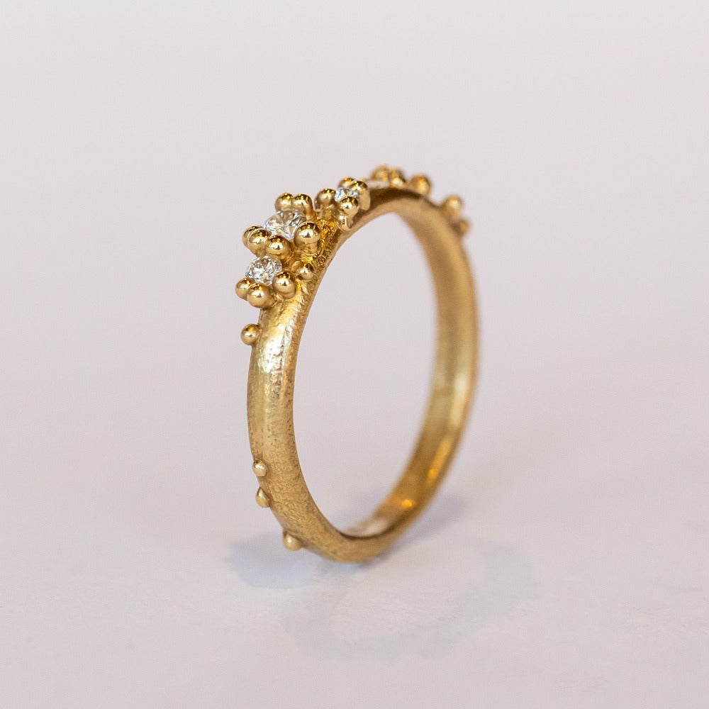 A stackable band featuring five white diamonds nestling amongst granules of yellow gold on a gently textured half round band.