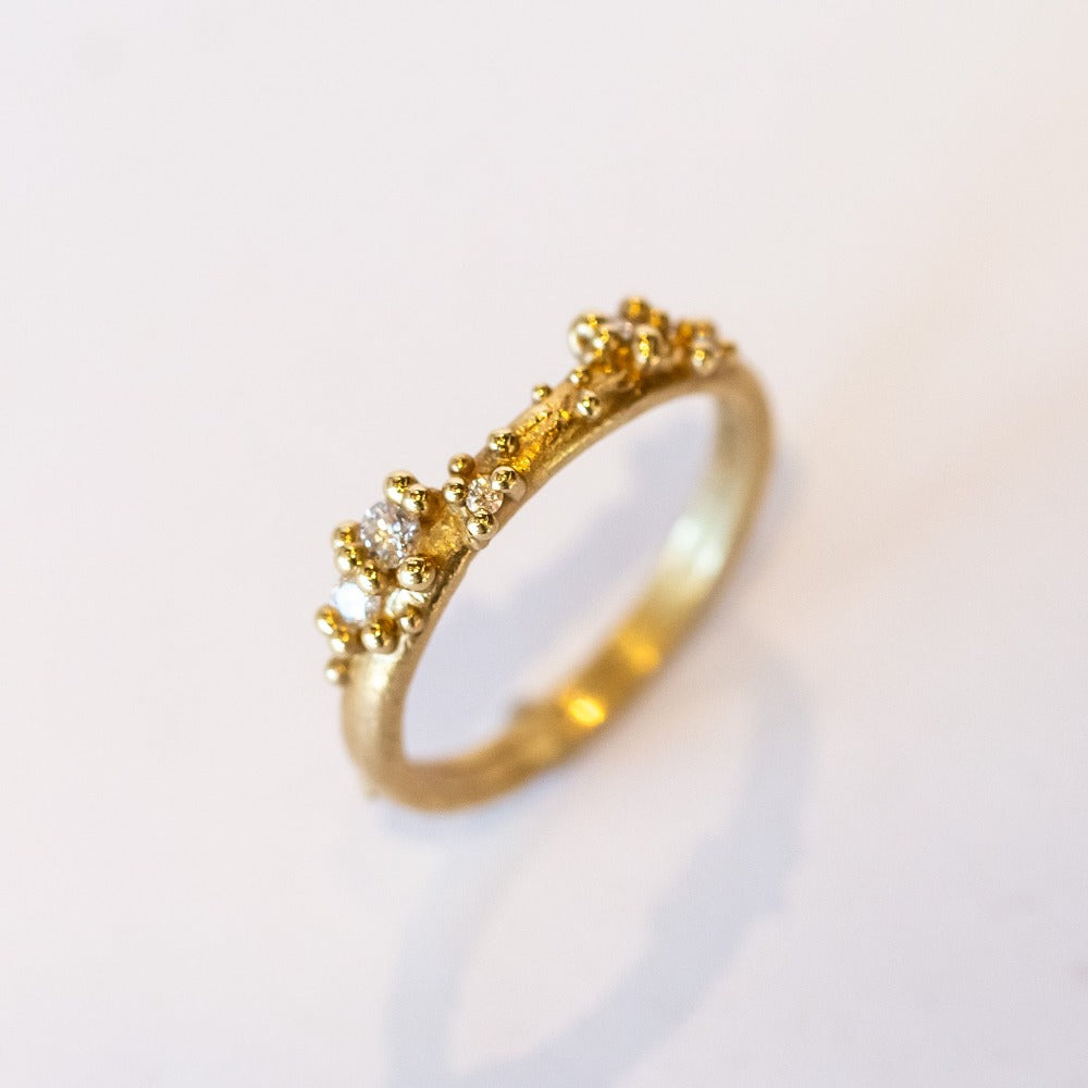 A stackable band featuring five white diamonds nestling amongst granules of yellow gold on a gently textured half round band.