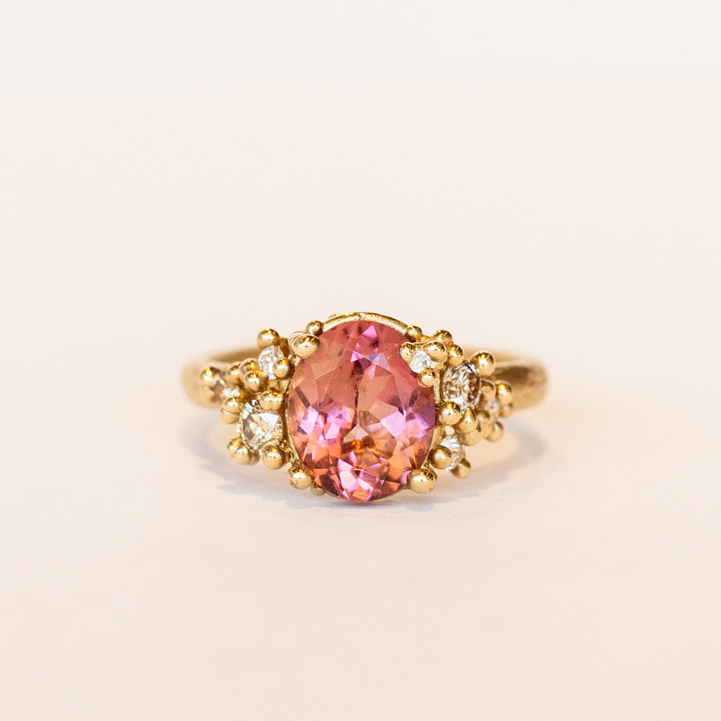 Oval peach-pink tourmaline set amongst&nbsp;golden granules and diamonds in yellow gold, on a gently textured band.