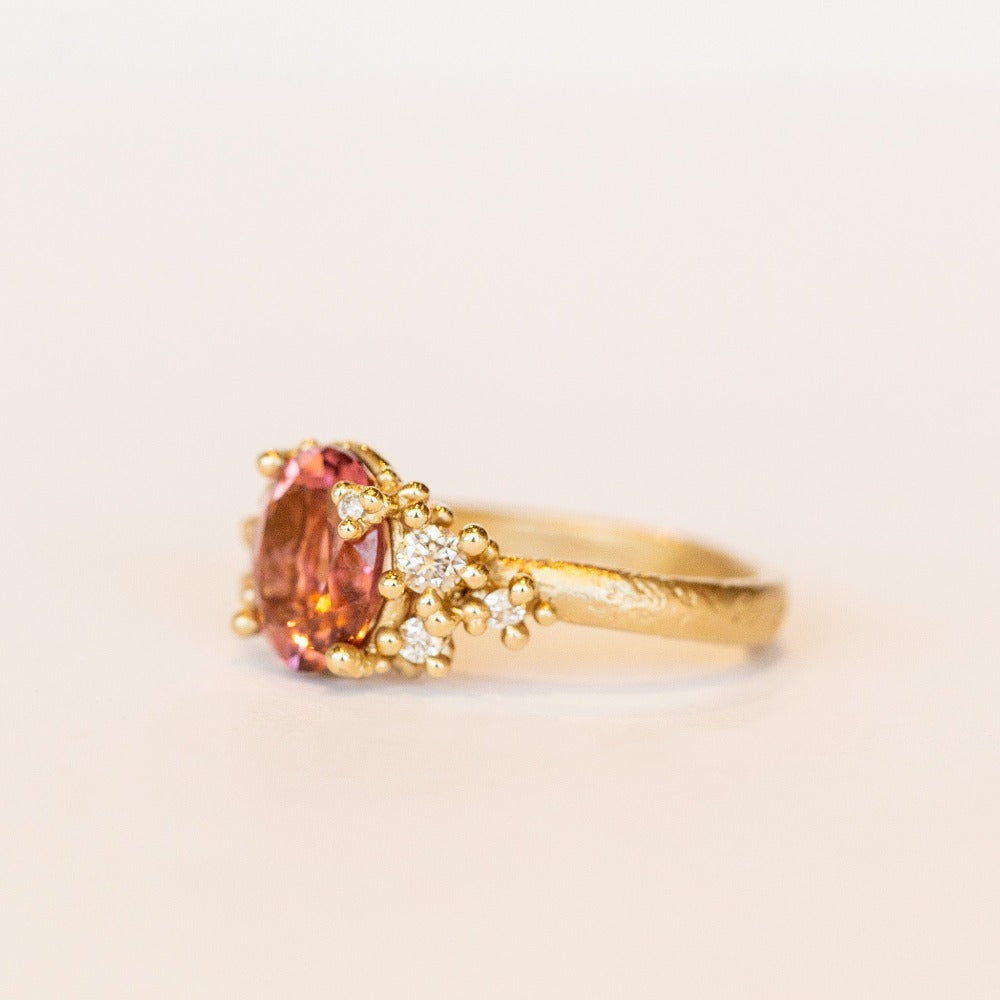 Oval peach-pink tourmaline set amongst&nbsp;golden granules and diamonds in yellow gold, on a gently textured band.