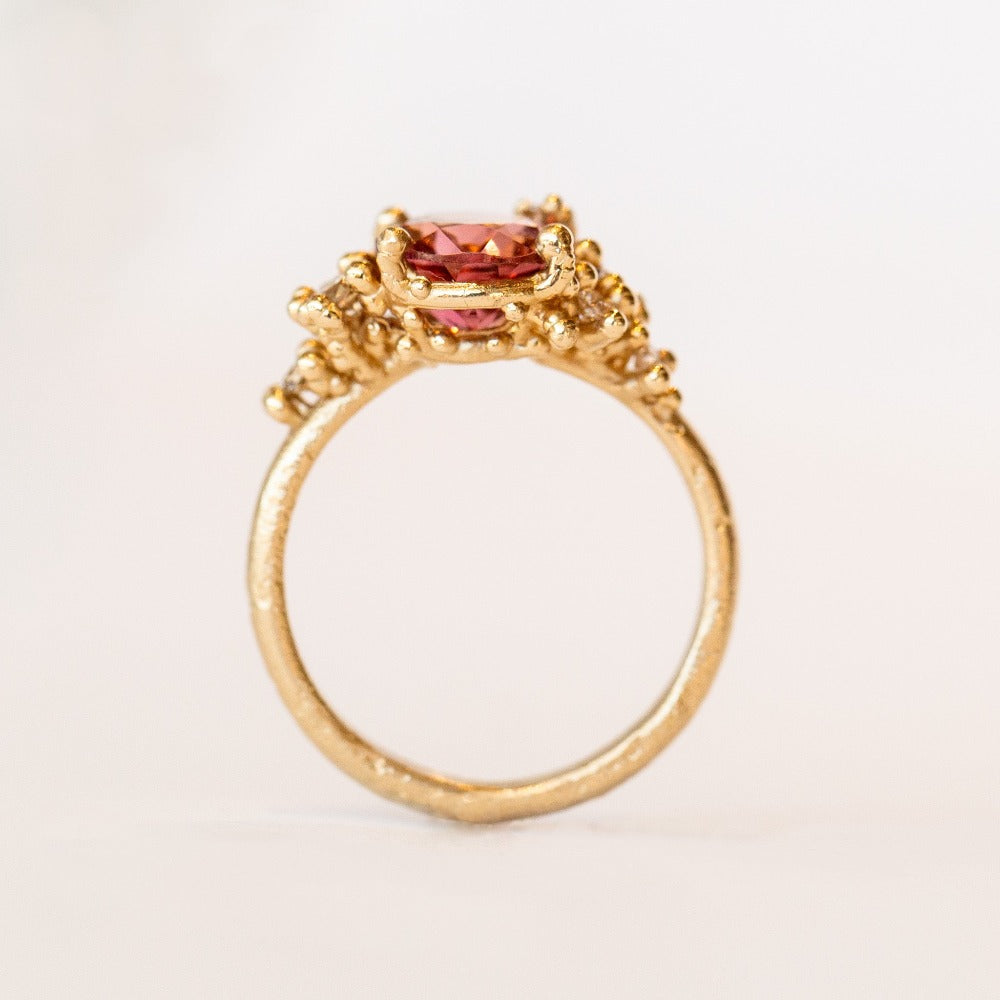 Oval peach-pink tourmaline set amongst&nbsp;golden granules and diamonds in yellow gold, on a gently textured band.