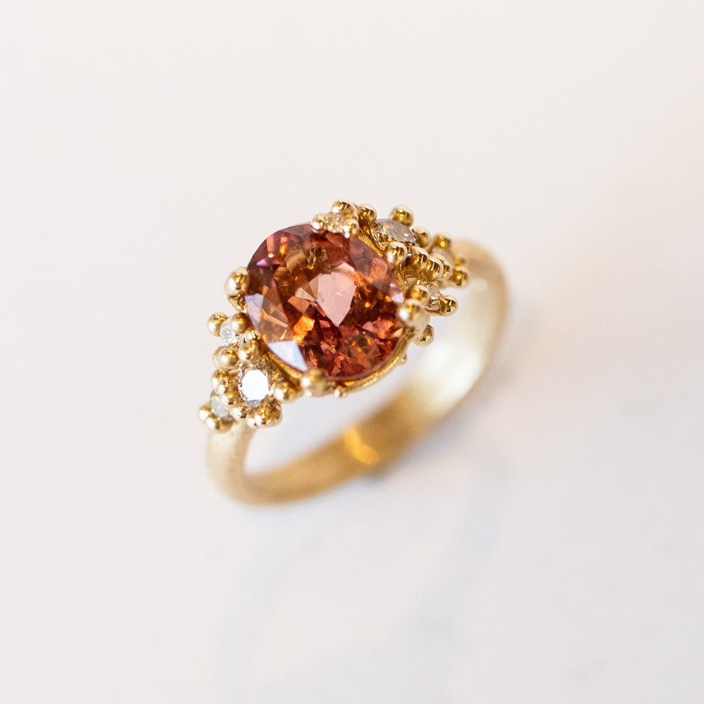 Oval peach-pink tourmaline set amongst&nbsp;golden granules and diamonds in yellow gold, on a gently textured band.