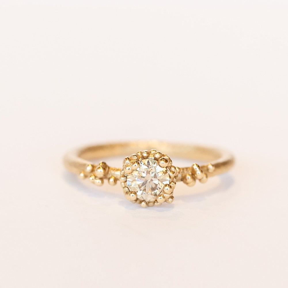 A round diamond solitaire engagement ring set in a granulated setting in yellow gold.