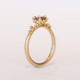 A round diamond solitaire engagement ring set in a granulated setting in yellow gold.