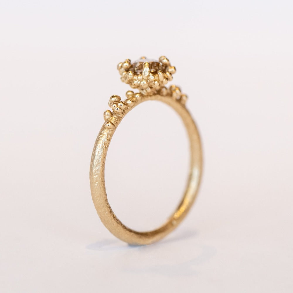 A round diamond solitaire engagement ring set in a granulated setting in yellow gold.