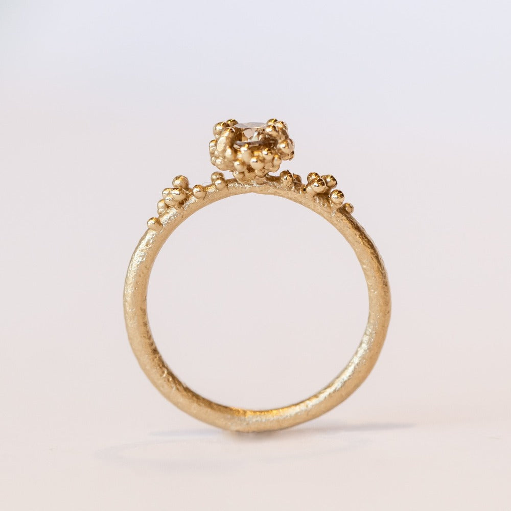 A round diamond solitaire engagement ring set in a granulated setting in yellow gold.