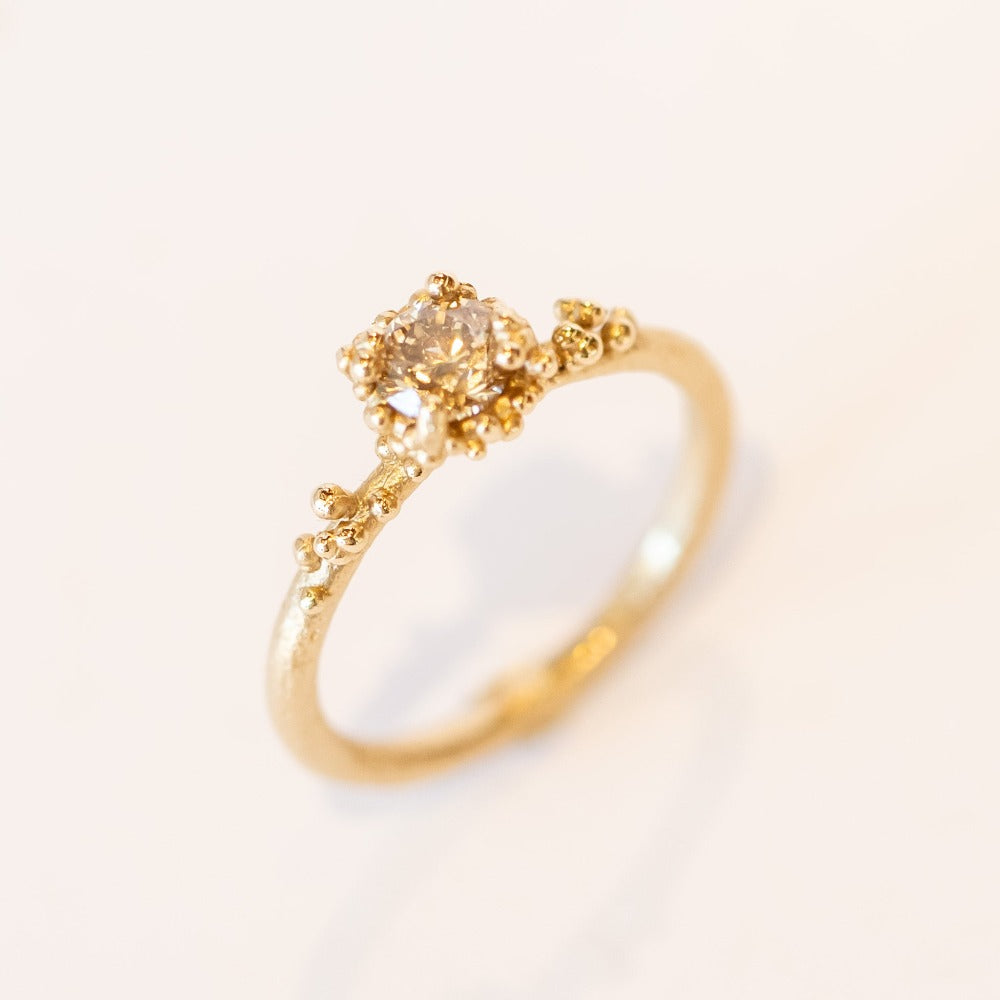 A round diamond solitaire engagement ring set in a granulated setting in yellow gold.