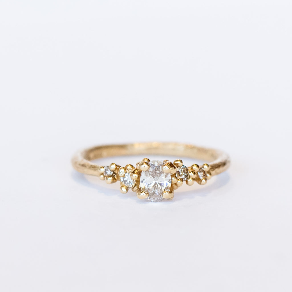 A unique engagement ring with classic style and a delicate silhouette. A central oval cut champagne diamond is set amongst&nbsp;golden granules and flanked by smaller champagne diamonds for added sparkle.