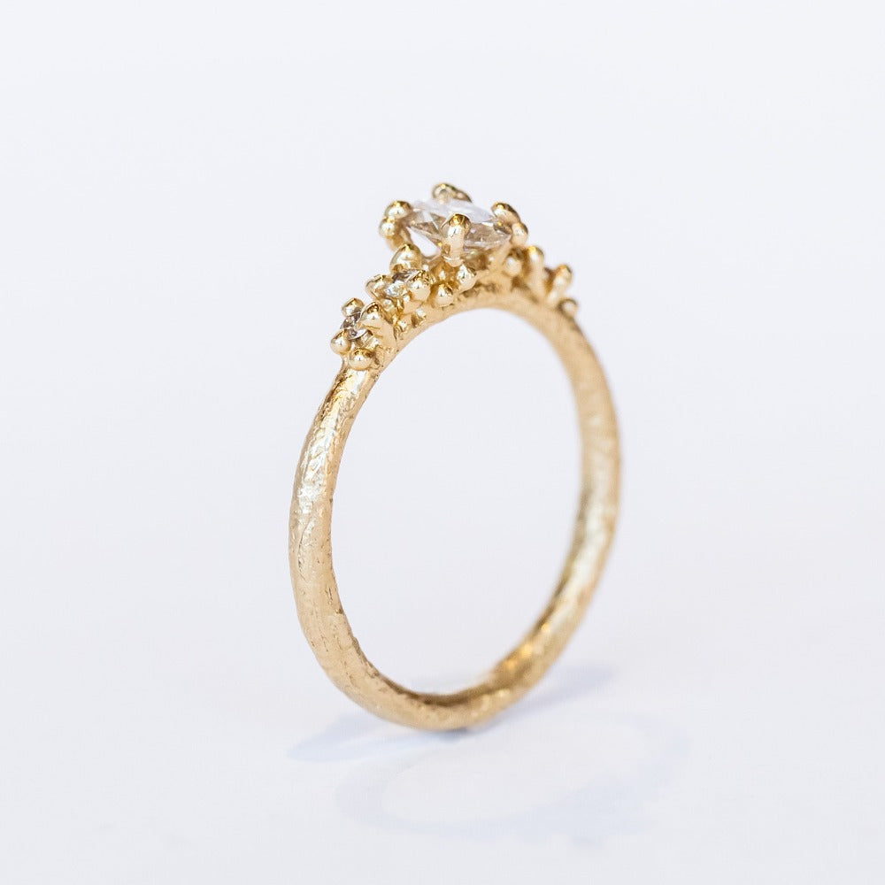 A unique engagement ring with classic style and a delicate silhouette. A central oval cut champagne diamond is set amongst&nbsp;golden granules and flanked by smaller champagne diamonds for added sparkle.