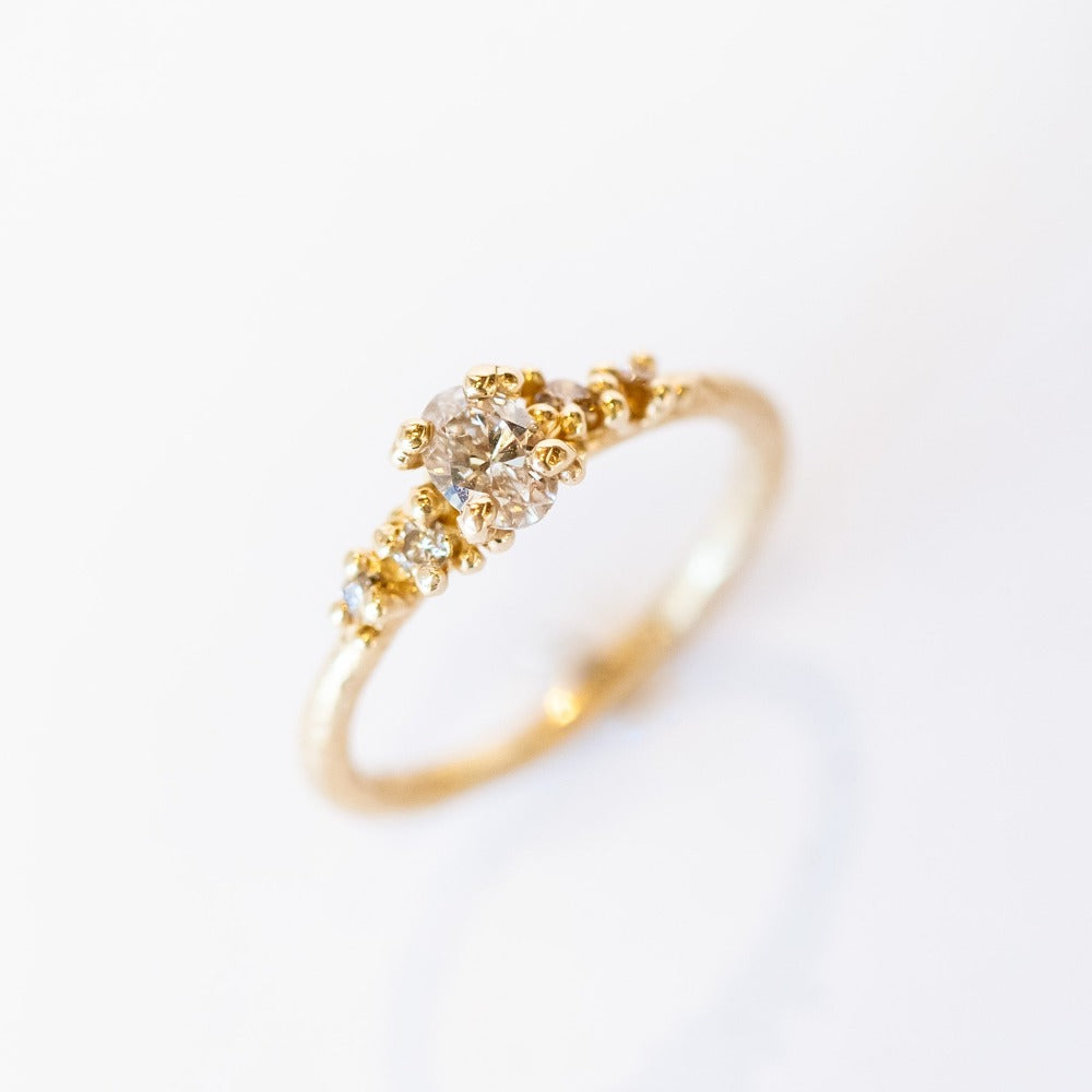 A unique engagement ring with classic style and a delicate silhouette. A central oval cut champagne diamond is set amongst&nbsp;golden granules and flanked by smaller champagne diamonds for added sparkle.