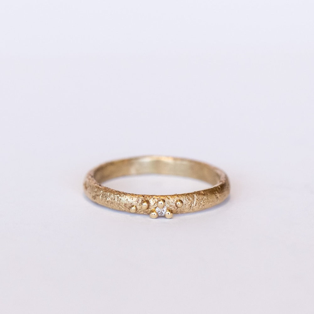 A textured yellow gold band with one tiny diamond set in gold granules.