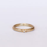 A textured yellow gold band with one tiny diamond set in gold granules.