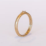 A textured yellow gold band with one tiny diamond set in gold granules.
