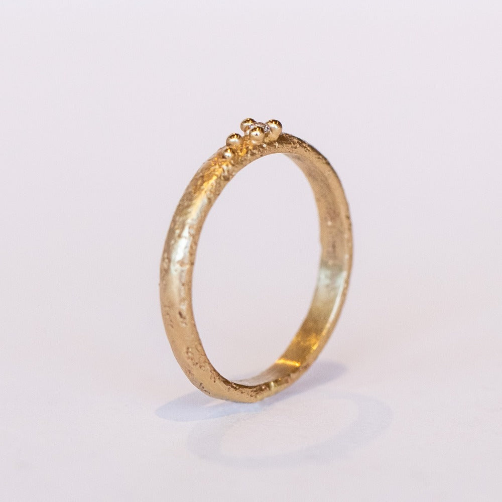 A textured yellow gold band with one tiny diamond set in gold granules.