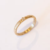 A textured yellow gold band with one tiny diamond set in gold granules.