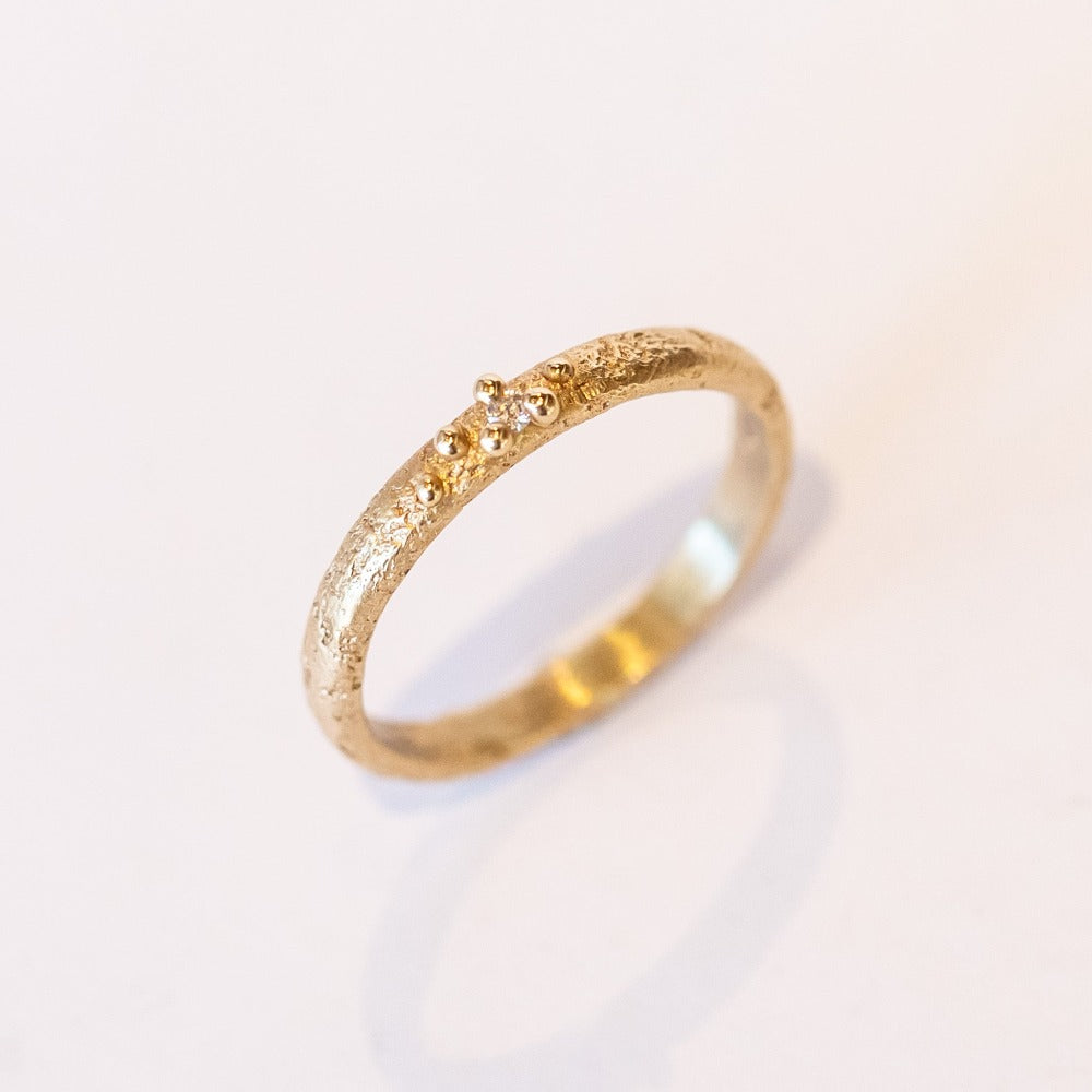 A textured yellow gold band with one tiny diamond set in gold granules.