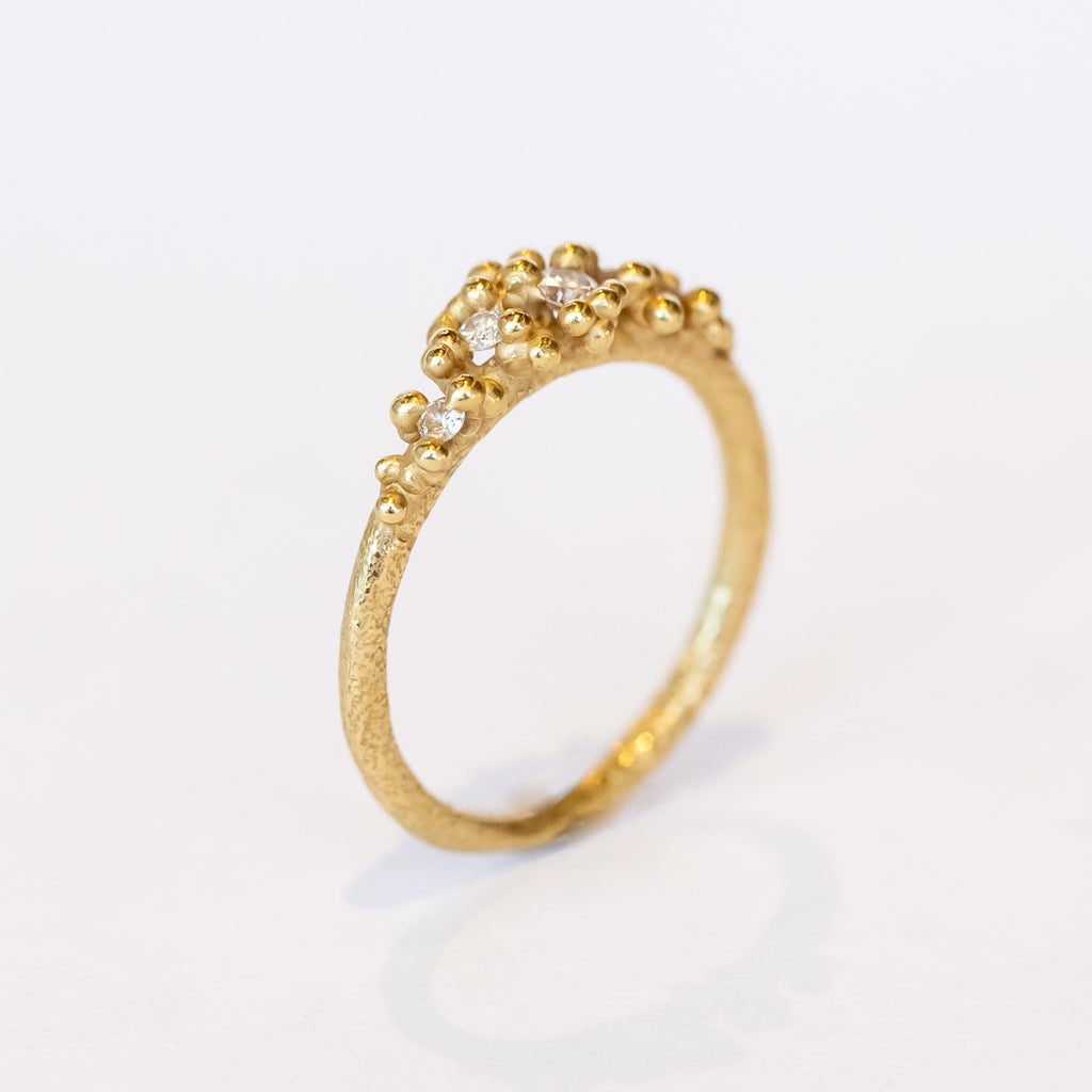 Unique diamond cluster engagement ring with golden granules, on a gently textured band.