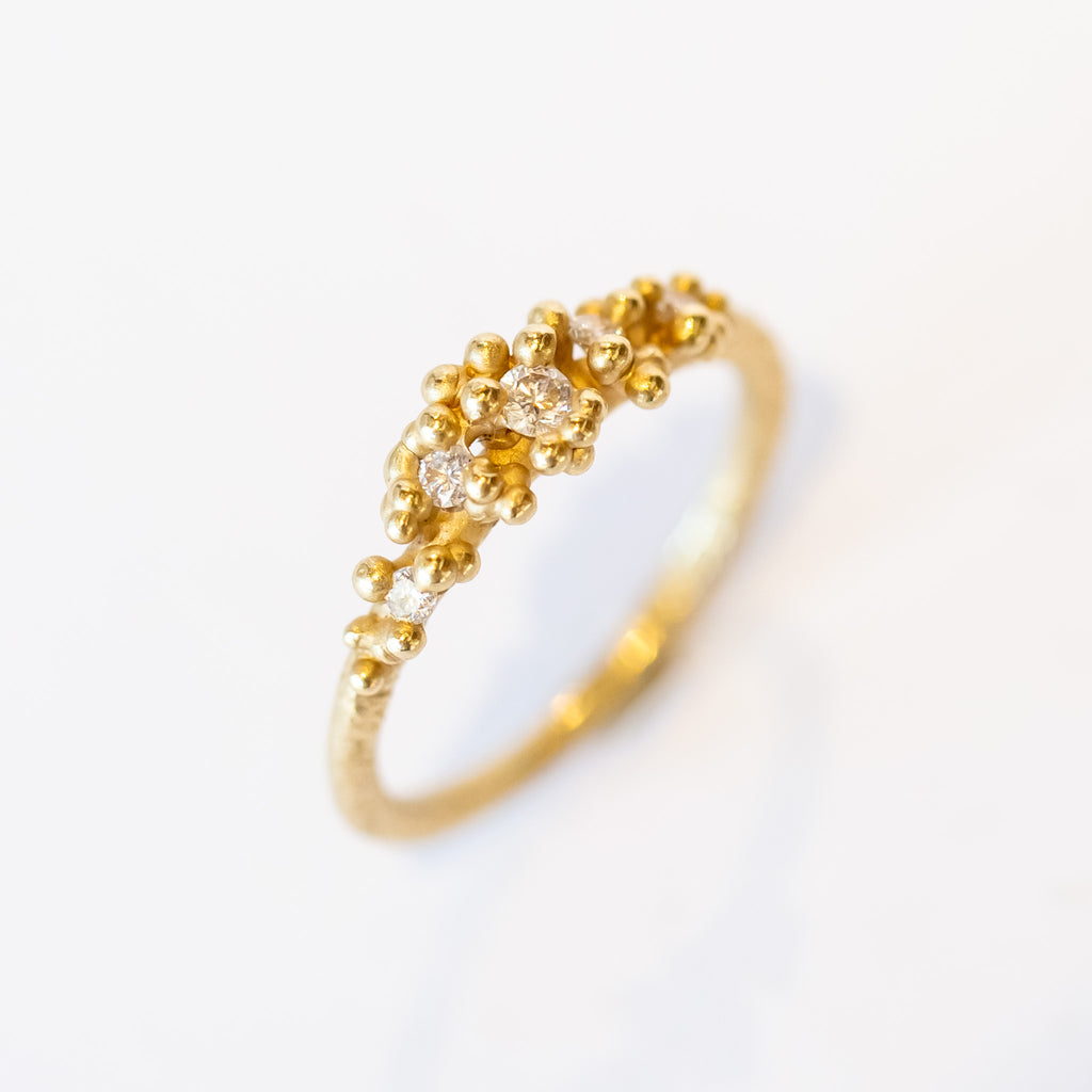 Unique diamond cluster engagement ring with golden granules, on a gently textured band.