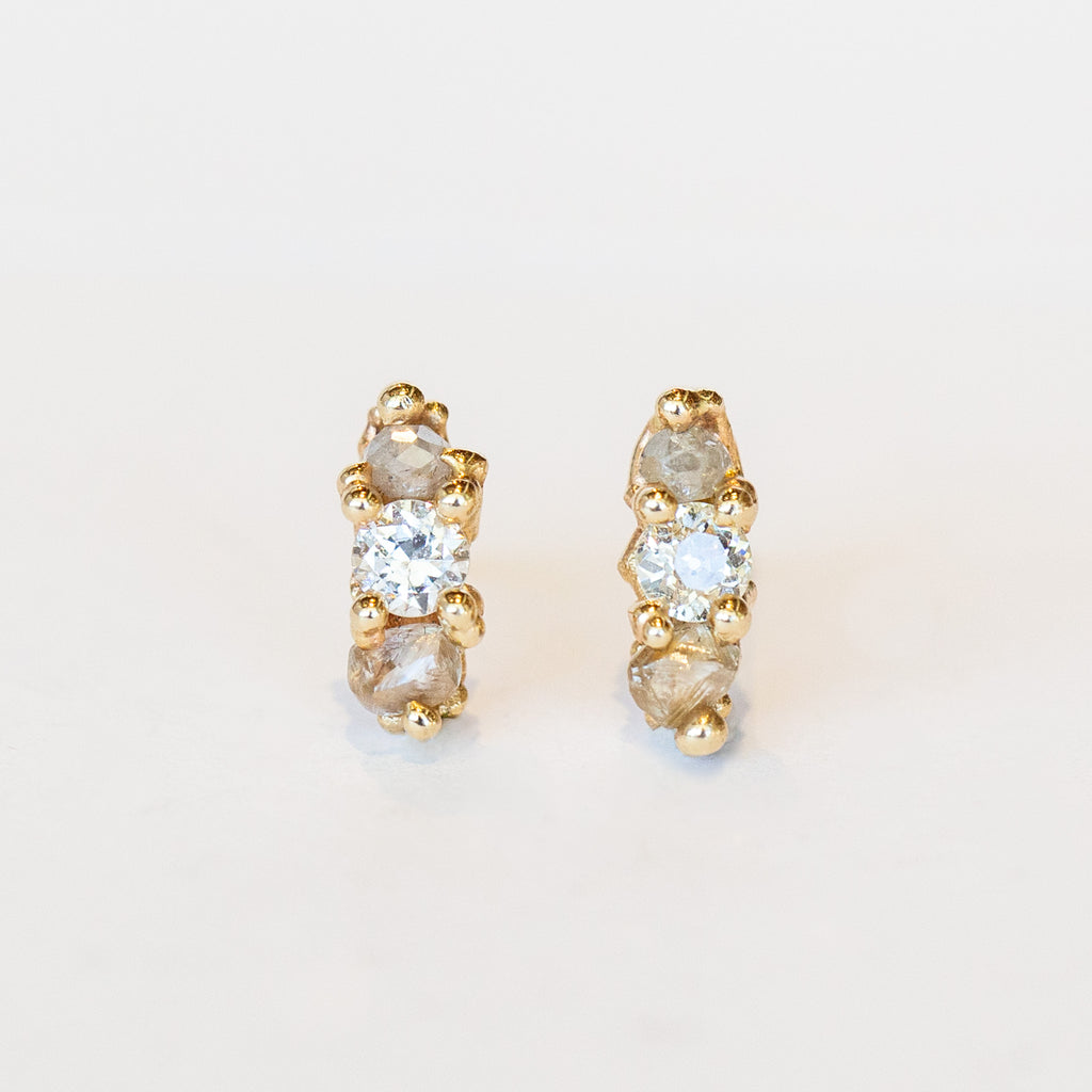 A pair of gold stud earrings set with white, grey, and champagne diamonds.