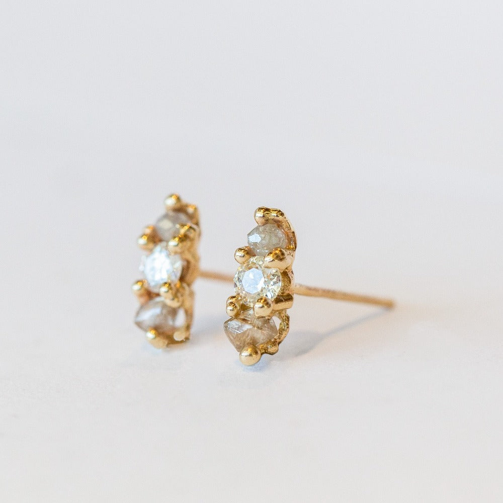 A pair of gold stud earrings set with white, grey, and champagne diamonds.