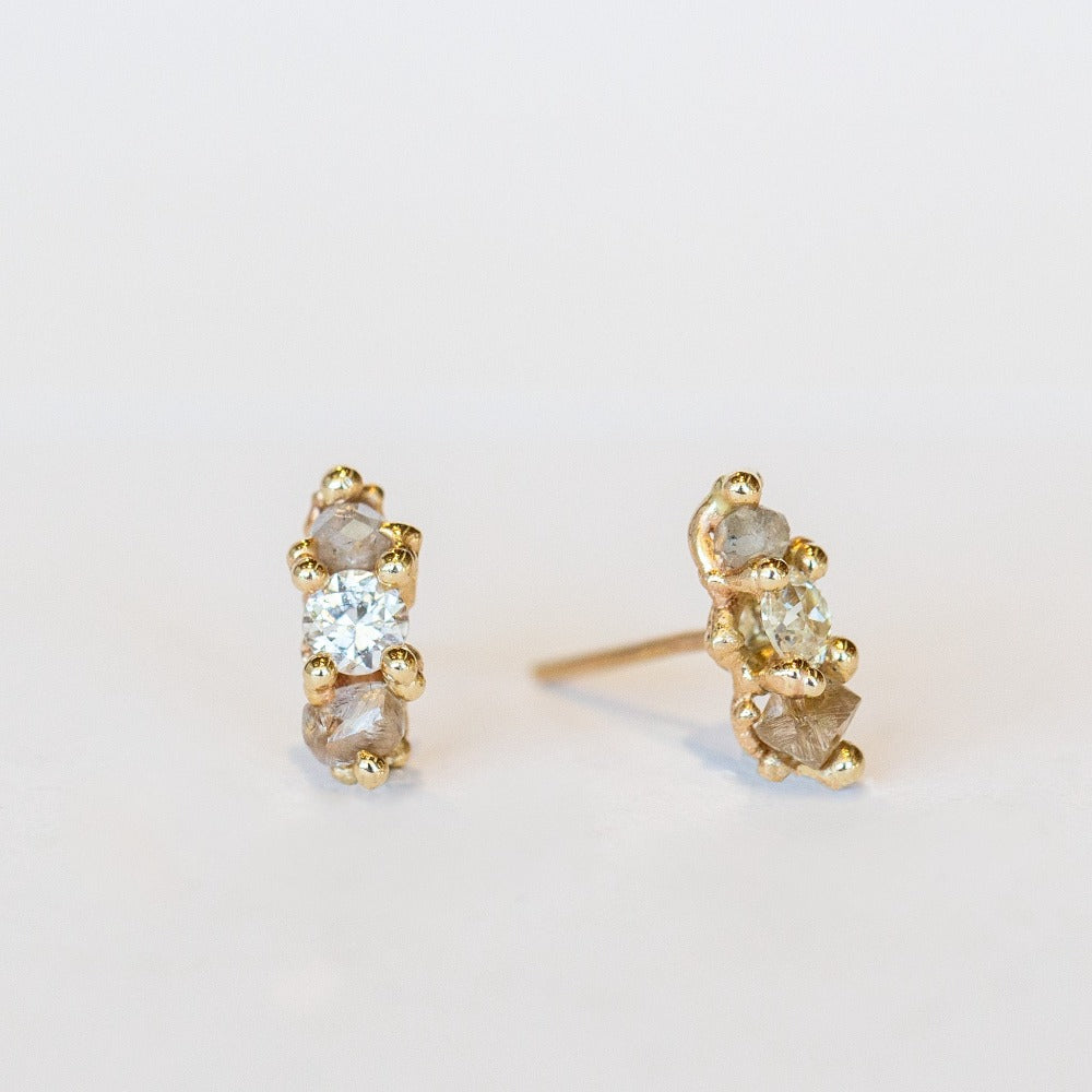 A pair of gold stud earrings set with white, grey, and champagne diamonds.