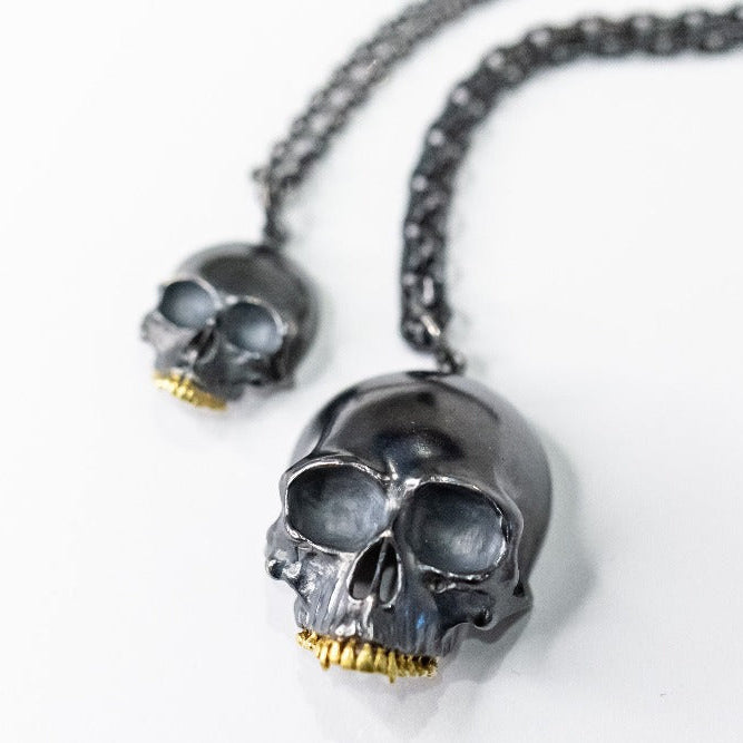 Two blackened silver skull pendants with gold teeth.