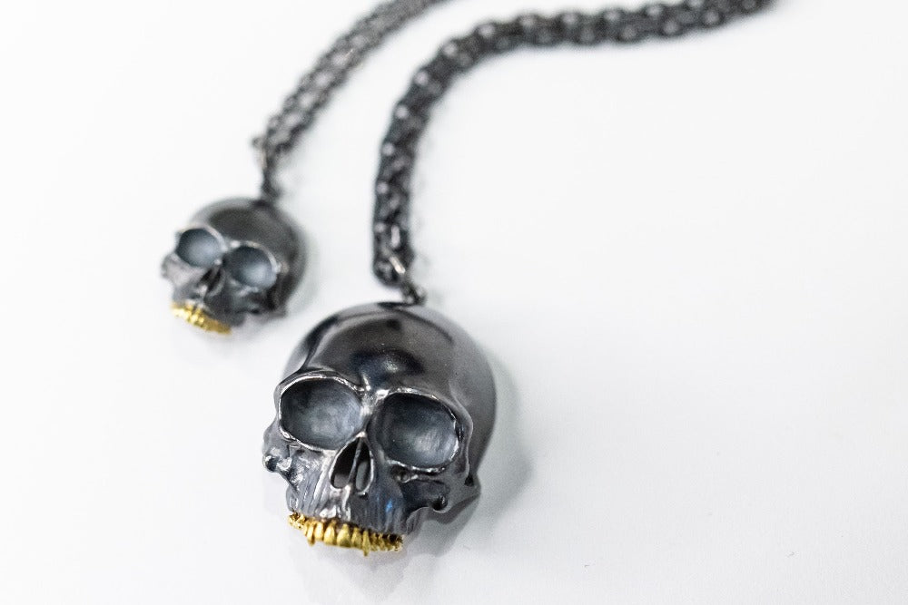Two blackened silver skull pendants with gold teeth.
