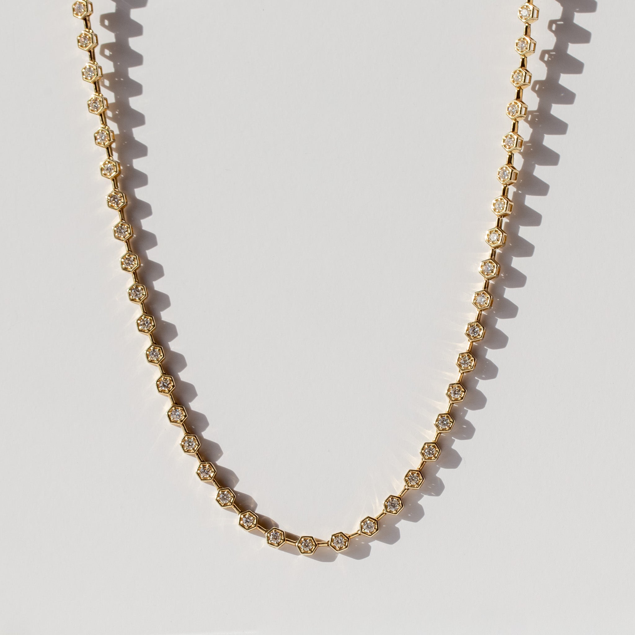 A diamond tennis necklace made up of hexagonal links each set with a small round diamond.
