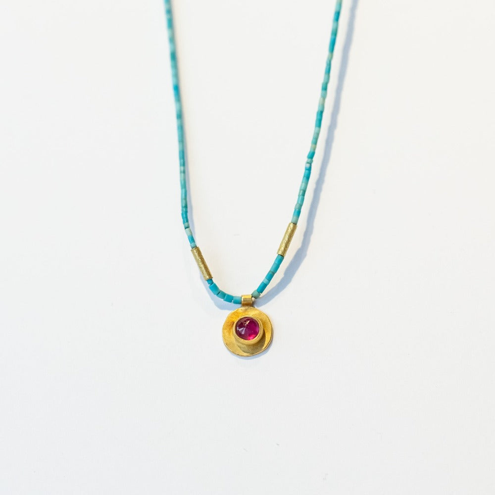 A thin, turquoise beaded necklace with a small ruby pendant set in yellow gold.