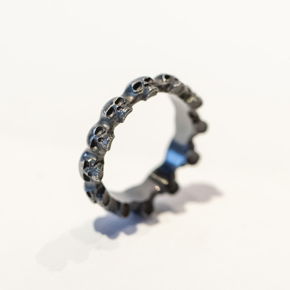 An eternity band of carved skulls made in blackened sterling silver.