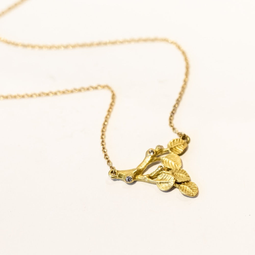 A carved branch pendant in yellow gold with a couple of tiny diamond accents, on a yellow gold chain.