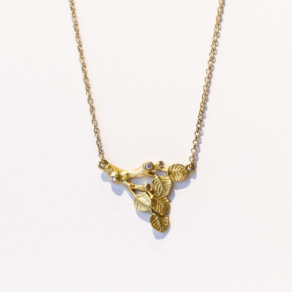 A carved branch pendant in yellow gold with a couple of tiny diamond accents, on a yellow gold chain.