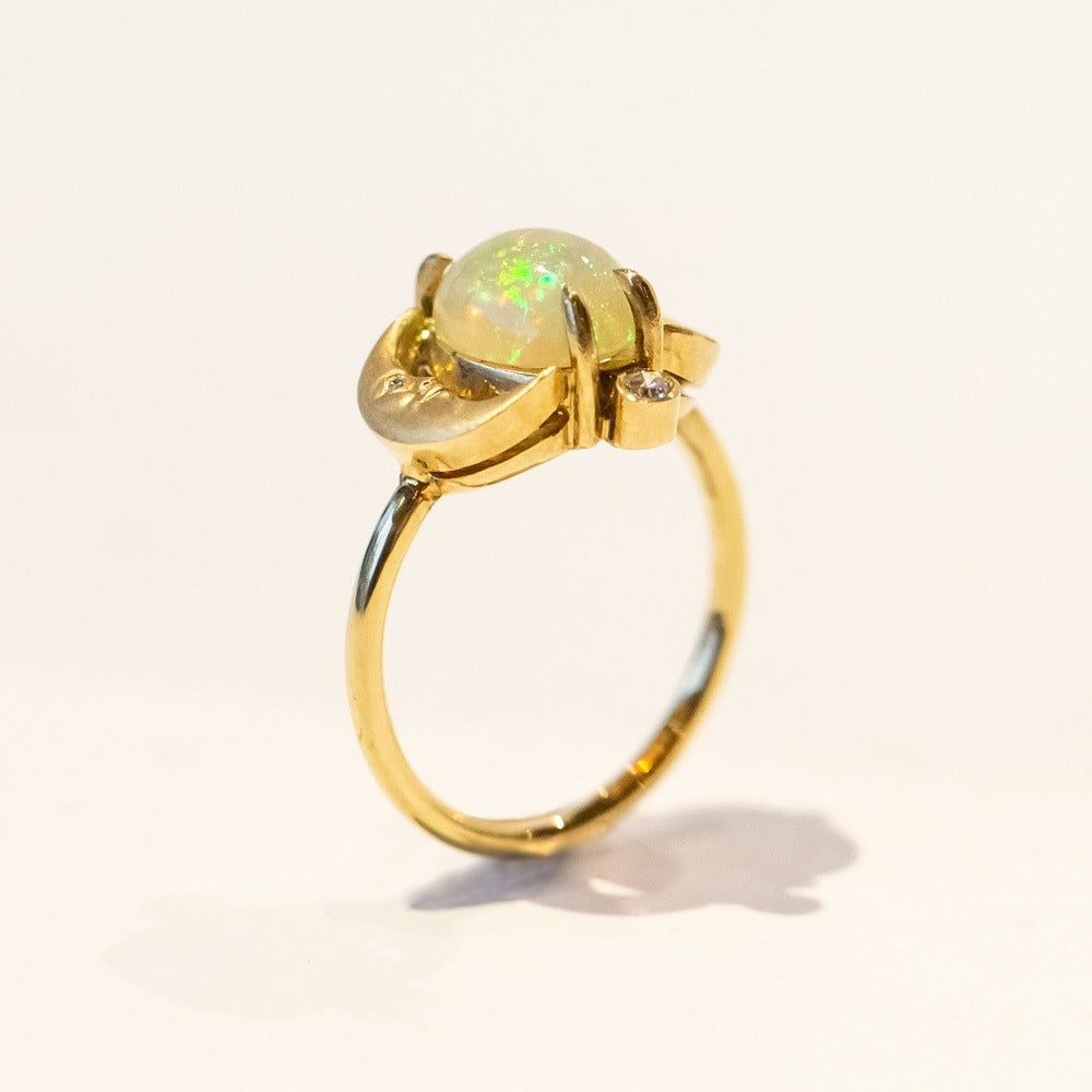 A yellow gold ring with an oval opal at its center, and facing moons on each side, accented by small diamonds.