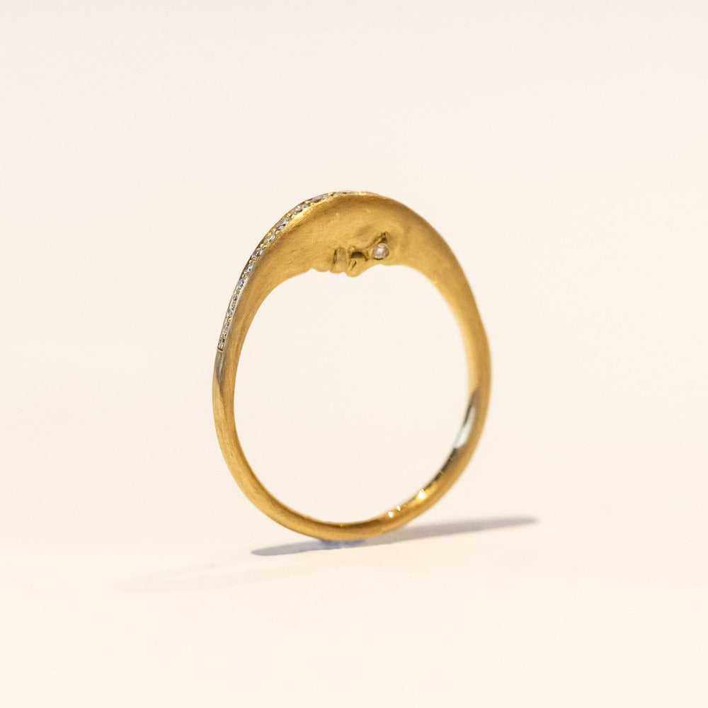 A carved yellow gold ring with a moon face that faces the finger and a row of diamonds along the outer edge.