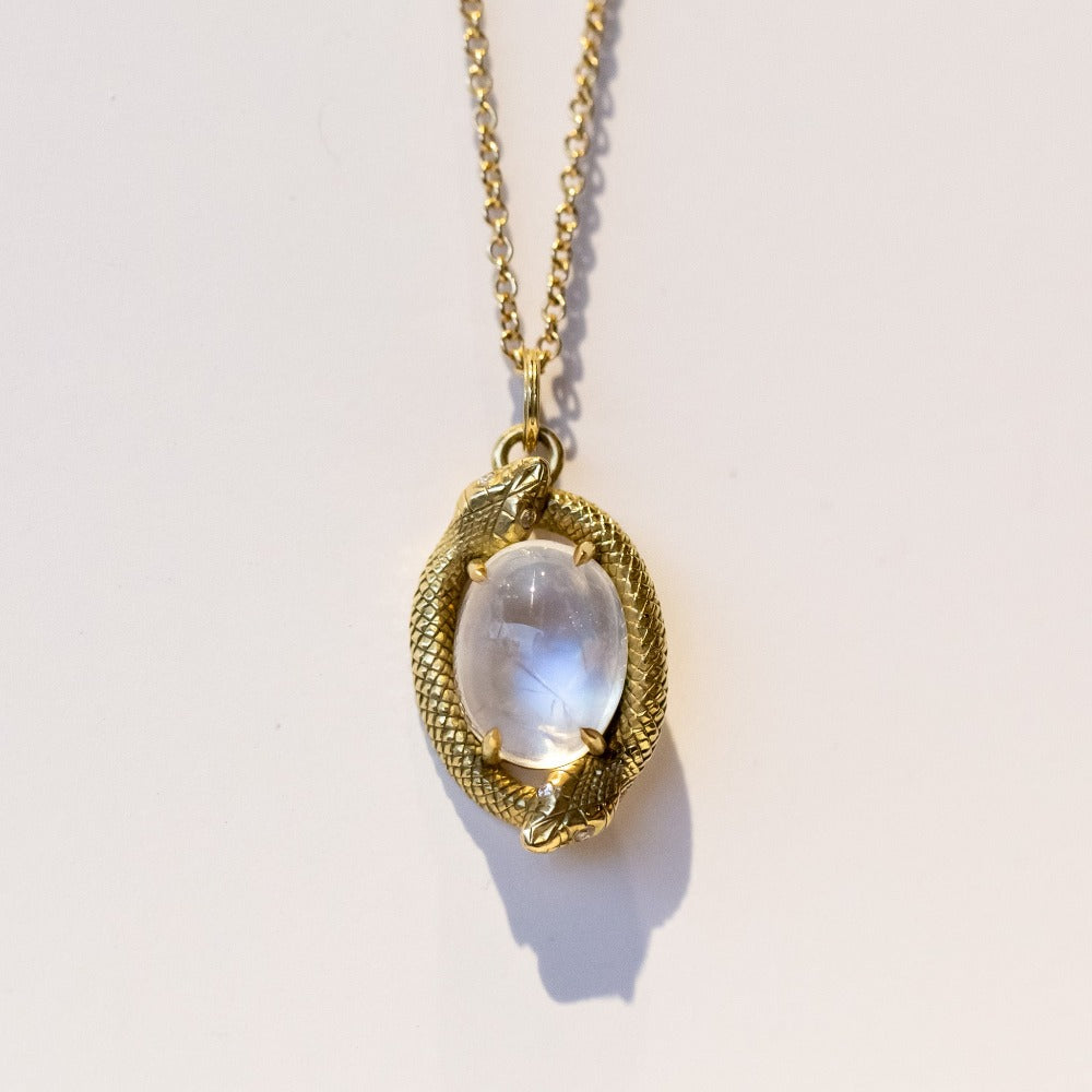 A pendant necklace featuring an oval moonstone at the center, encircled by two gold snakes in an ouroboros motif.