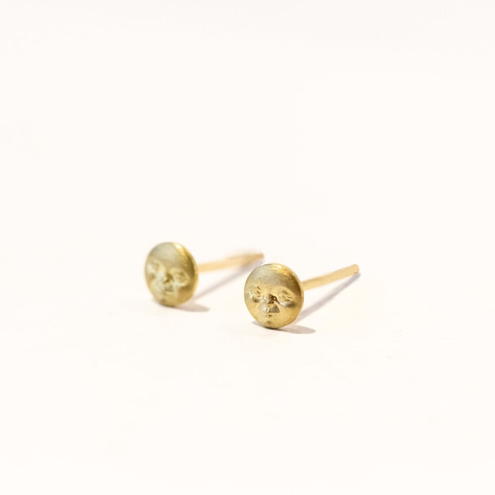Tiny full moon gold stud earrings with faces, angle view.