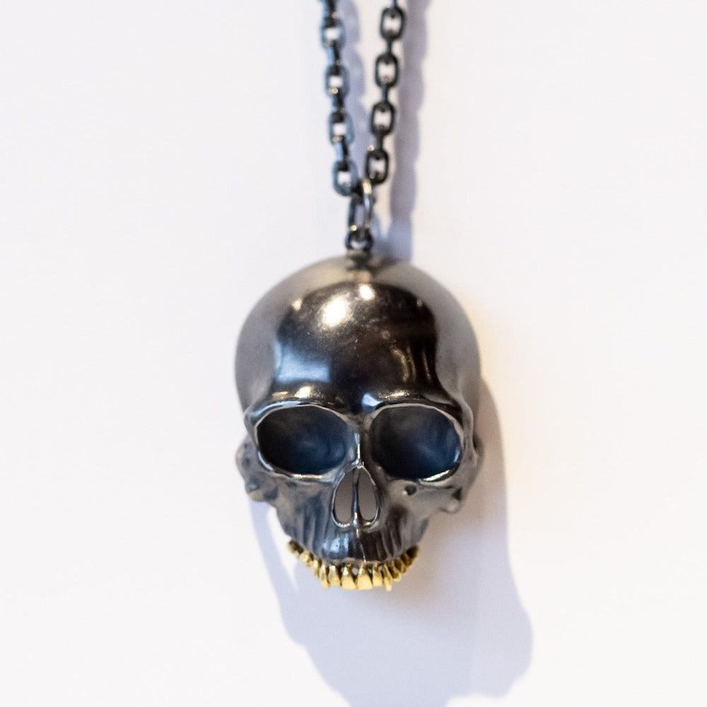 A large blackened silver skull pendant necklace with yellow gold teeth.