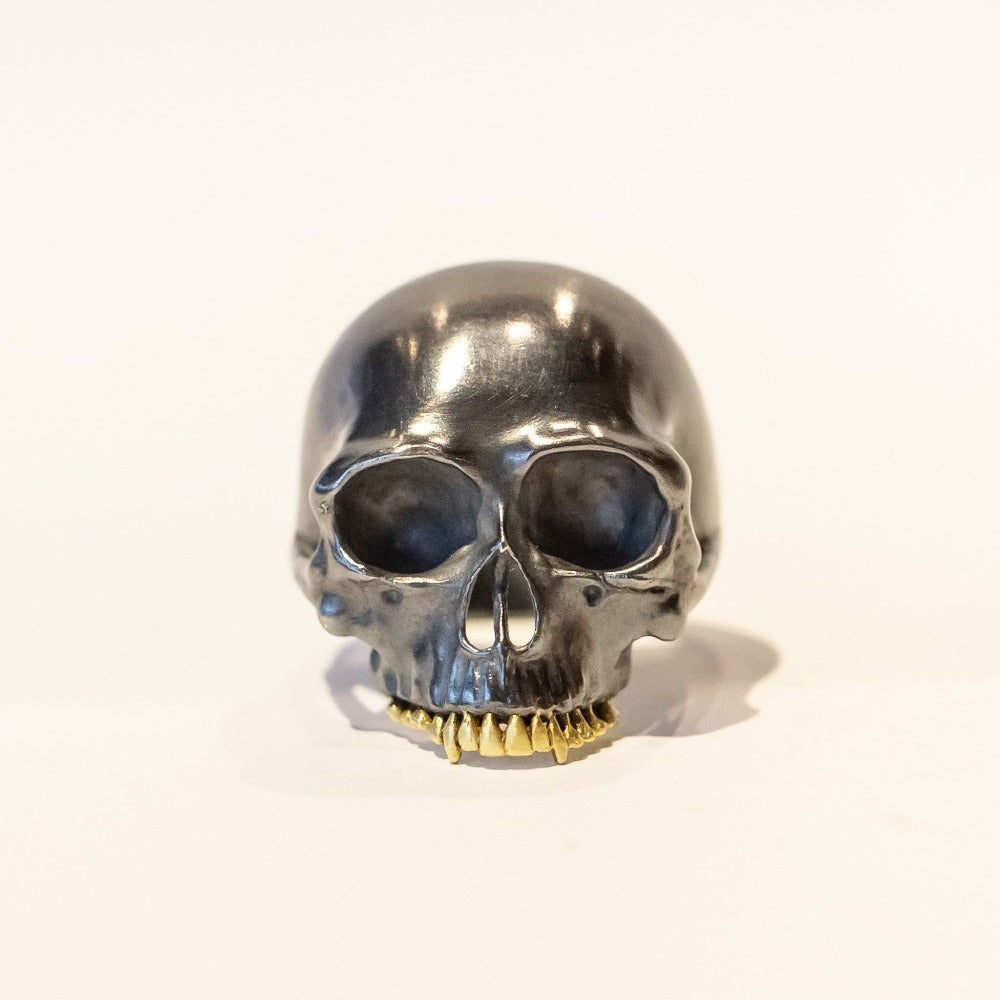 A large blackened silver carved skull ring with yellow gold teeth, front view.