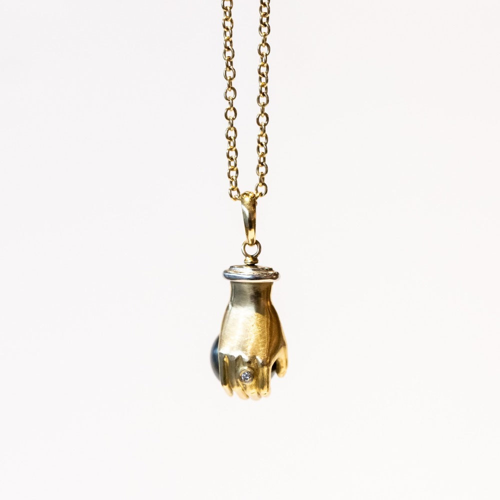 A yellow gold carved hand pendant holding a black Tahitian pearl.