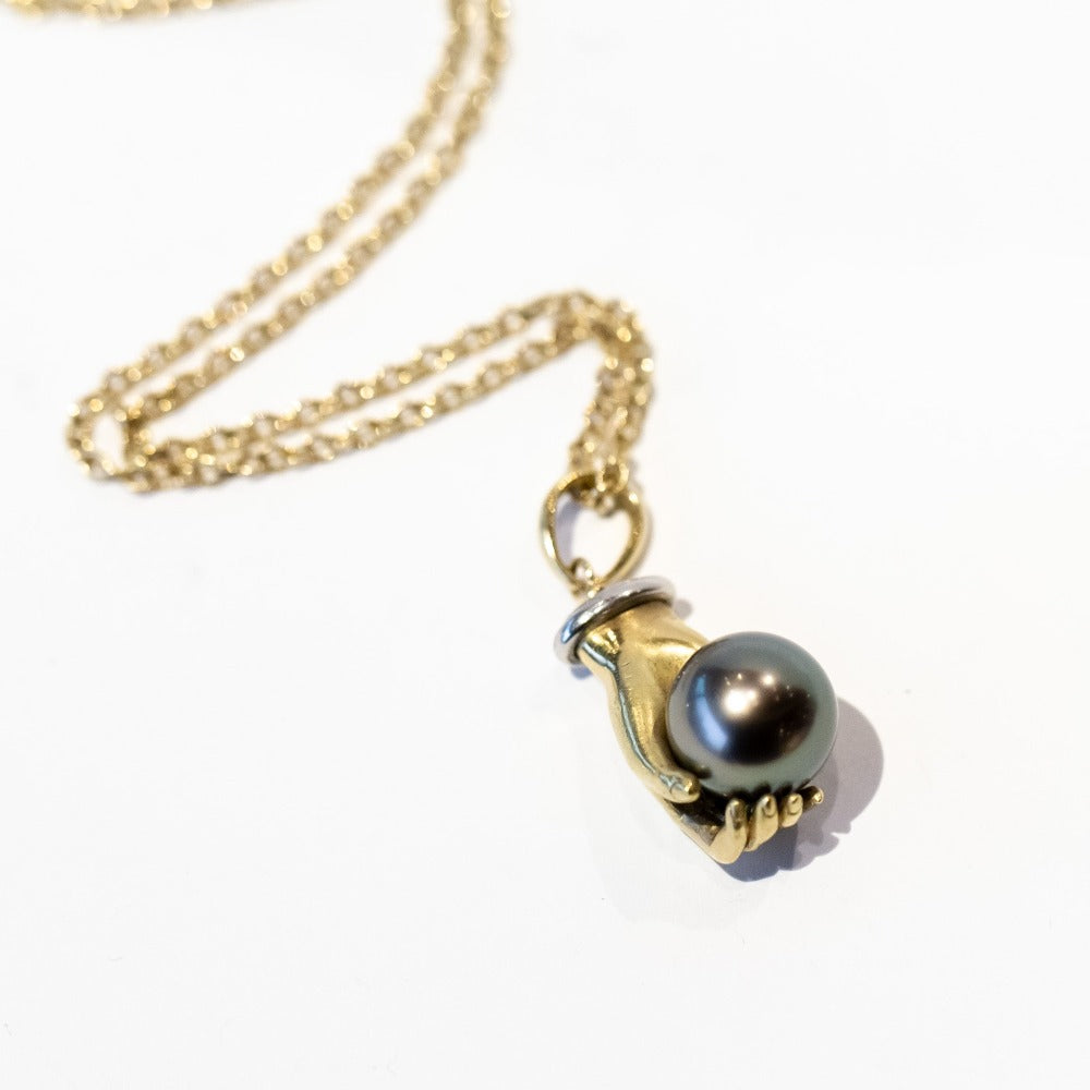 A yellow gold carved hand pendant holding a black Tahitian pearl.