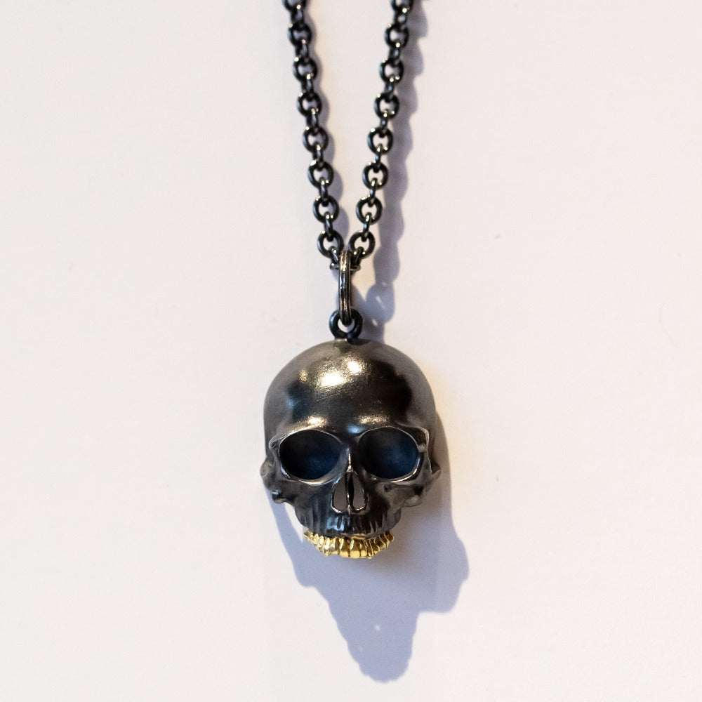 A blackened silver, carved skull pendant with yellow gold teeth.