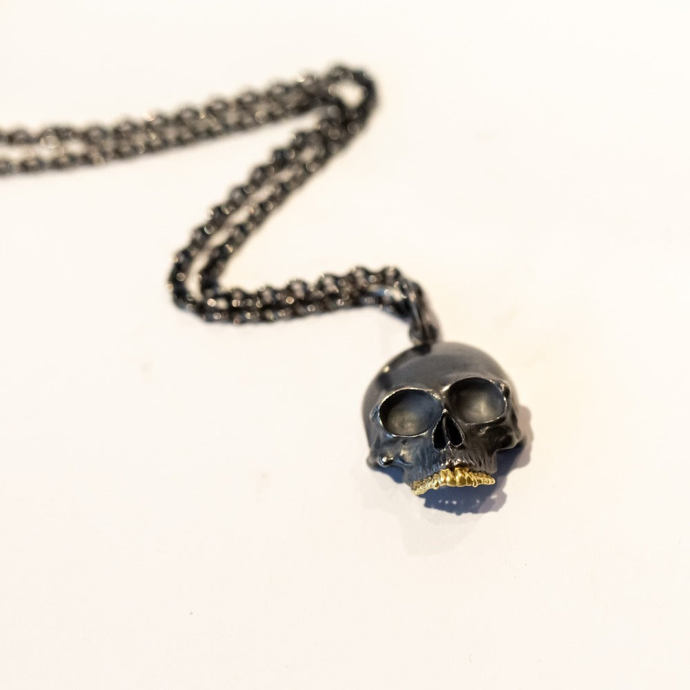 A blackened silver, carved skull pendant with yellow gold teeth.