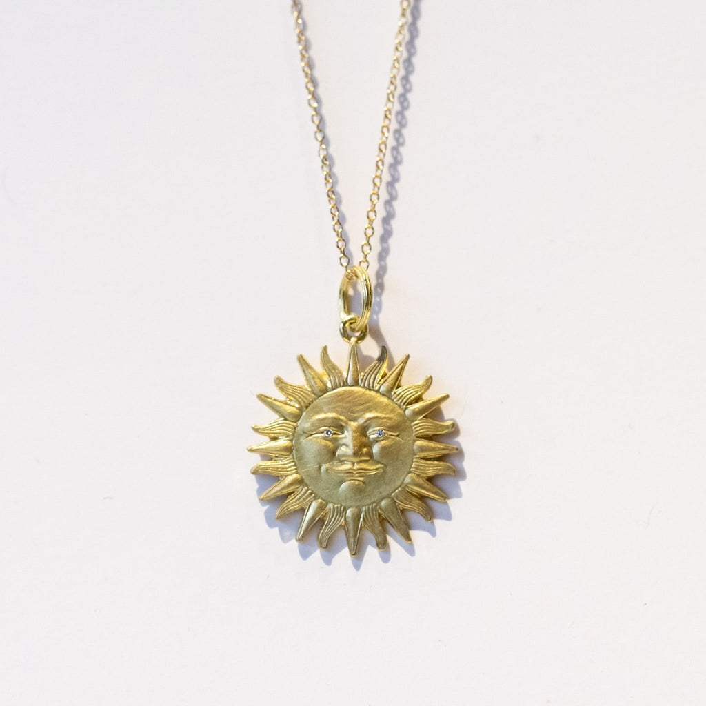 A carved sun pendant with face and diamond eyes in yellow gold.