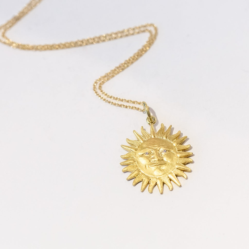A carved sun pendant with face and diamond eyes in yellow gold.