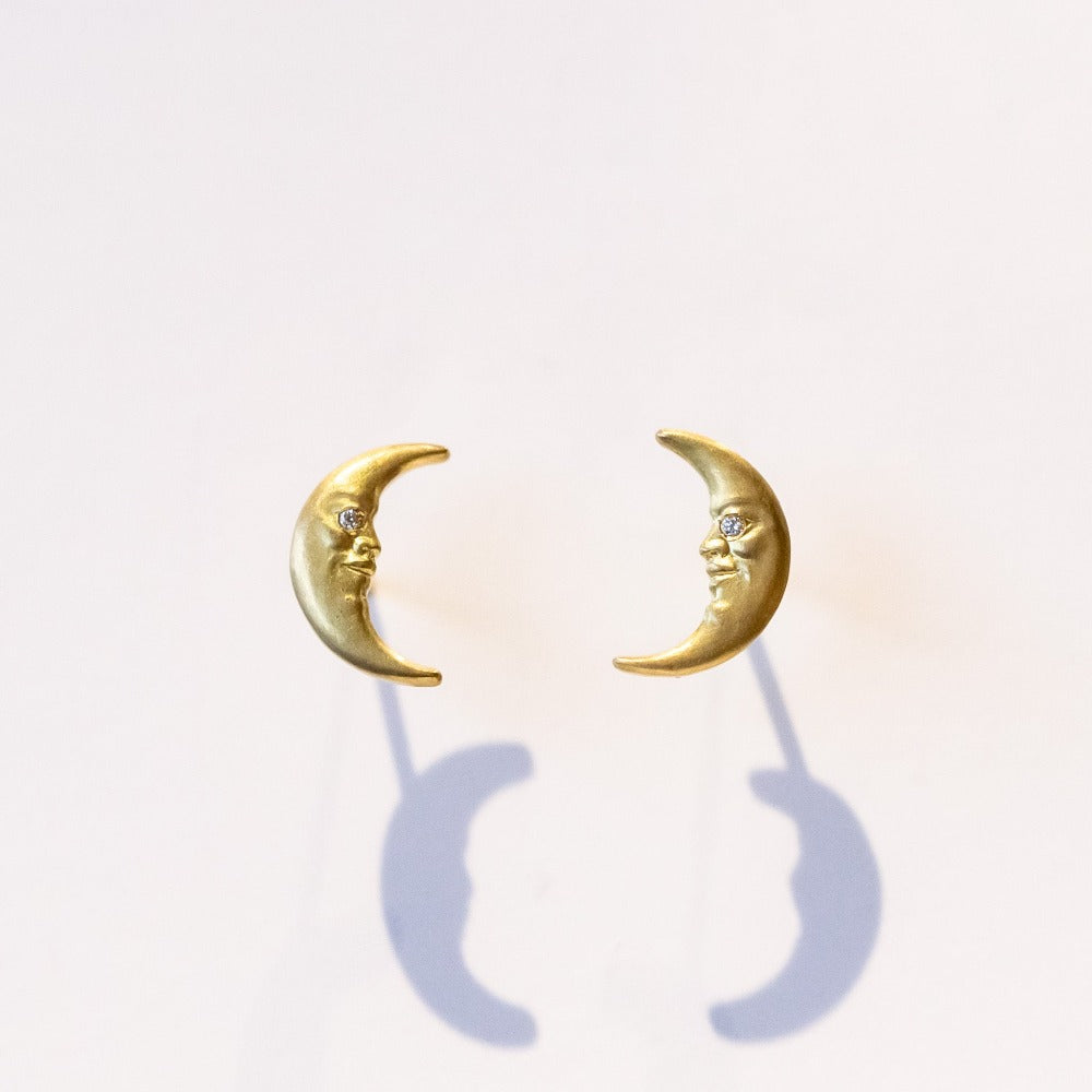 Crescent-moon shaped yellow gold stud earrings with faces and diamond eyes.