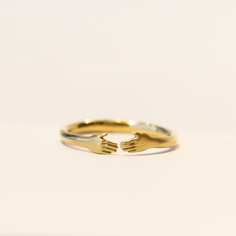 A dainty gold Anthony Lent ring featuring two tiny hands facing each other at the center.