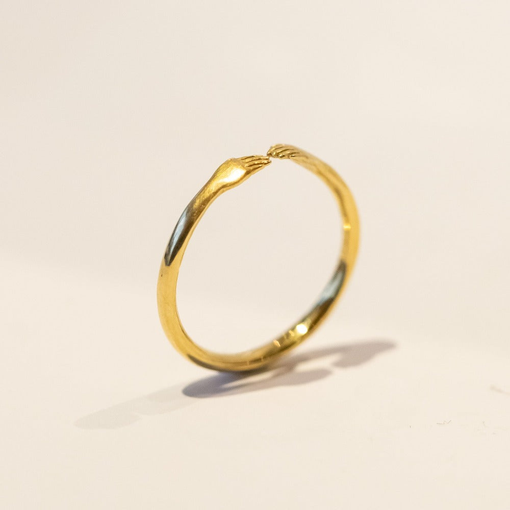 A dainty gold Anthony Lent ring featuring two tiny hands facing each other at the center.