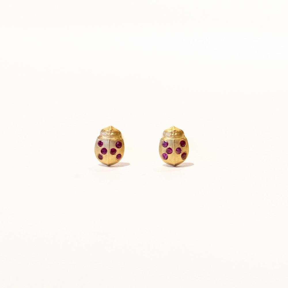 A pair of tiny yellow gold, ladybug shaped stud earrings with ruby spots on its wings.