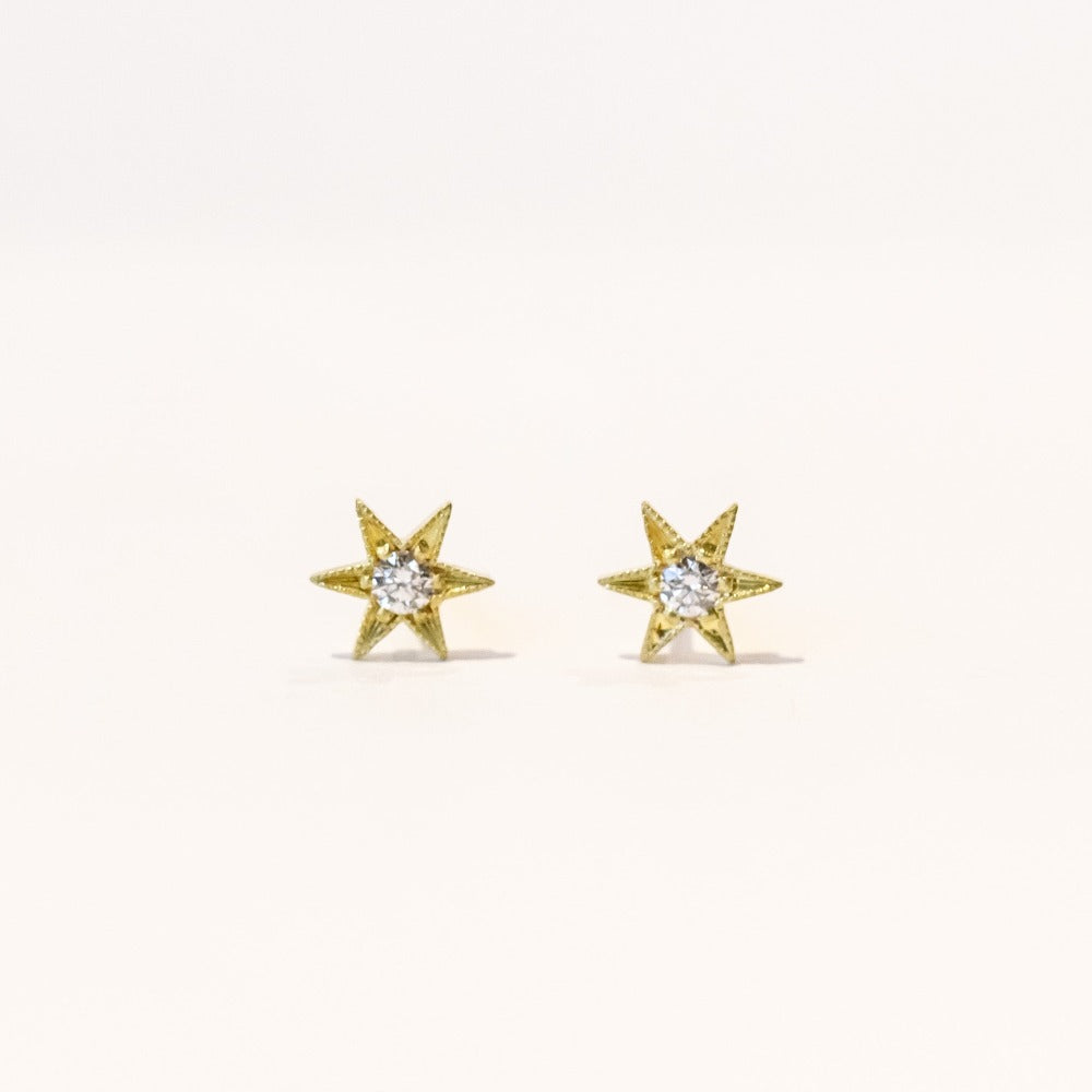 Tiny six-pointed gold star stud earrings with diamonds at their center.