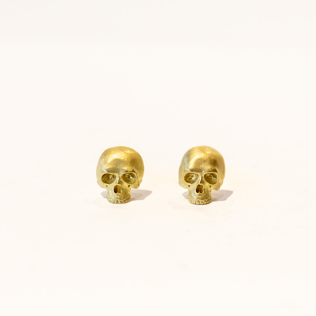 A pair of tiny, carved yellow gold skull shaped stud earrings.